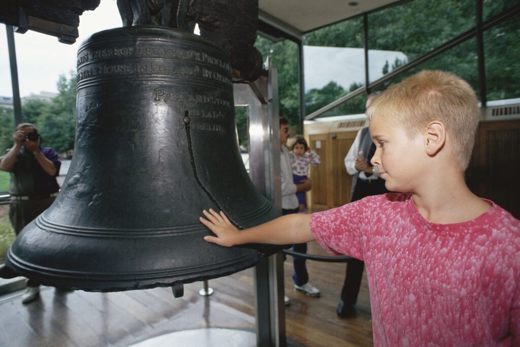20738199 - boy putting his hand on liberty bell