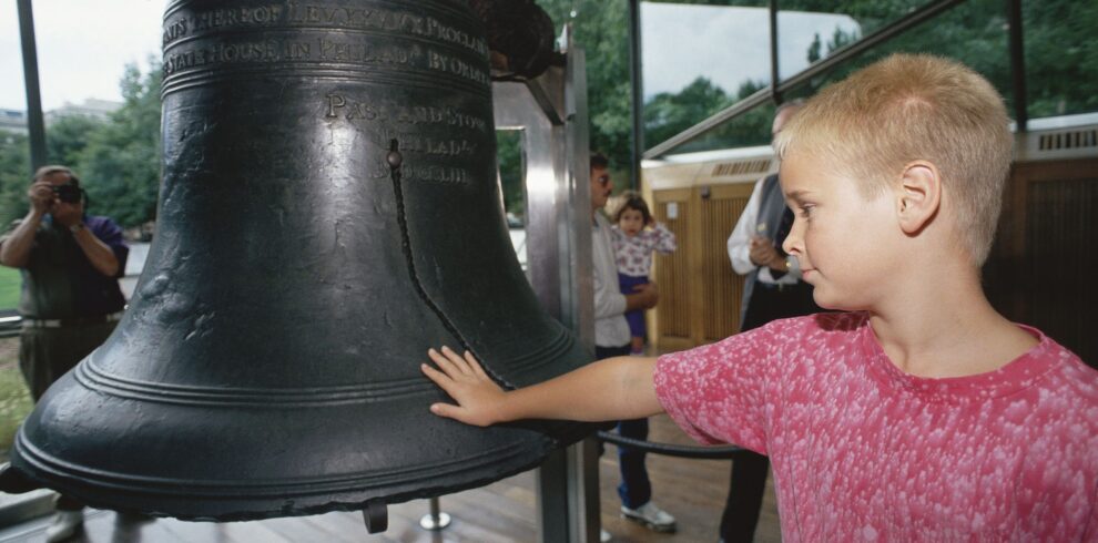 20738199 - boy putting his hand on liberty bell